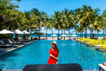 Travel vacation woman in red dress enjoying a summer vacation near swimming pool in tropical resort...