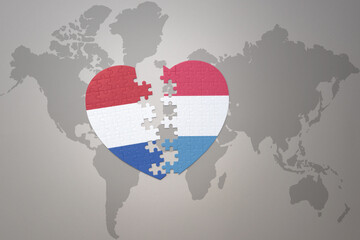 puzzle heart with the national flag of luxembourg and netherlands on a world map background.Concept.