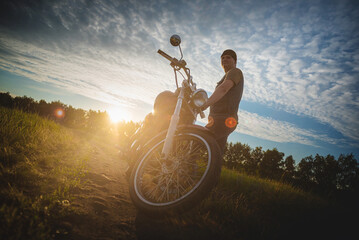 Motorbiker on the motorbike on the dusty empty countryside road at the sunset sun background. Motorcycle travel.