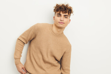 horizontal photo of a cute, pleasant man in a beige sweater looking at the camera while posing relaxed