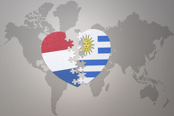 Fototapeta premium puzzle heart with the national flag of uruguay and netherlands on a world map background.Concept.