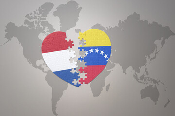 puzzle heart with the national flag of venezuela and netherlands on a world map background.Concept.
