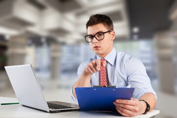 Smiling young businessman sitting at worktable at modern office,