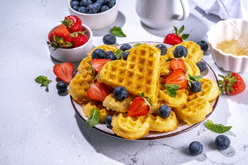 Breakfast belgian waffles with strawberries, blueberries and honey, homemade healthy heart shaped waffles on white kitchen tables copy space