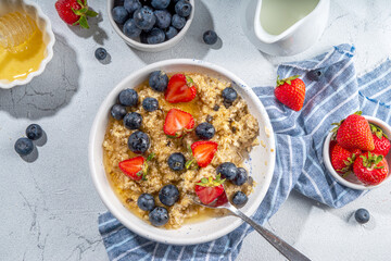Summer morning oatmeal with berry. Homemade healthy breakfast oats with strawberry, blueberry, honey, nuts and mint on white marble background