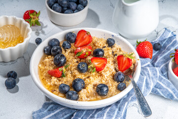 Summer morning oatmeal with berry. Homemade healthy breakfast oats with strawberry, blueberry, honey, nuts and mint on white marble background