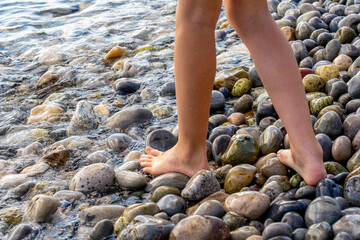 A girl's feet walk along pebble coast of the sea. The girl's legs close up. Hight quality photo