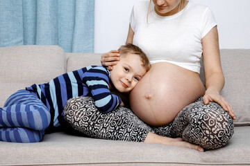 Child hugs her mother's pregnant belly. Happy family life in an expectation a newborn. Pregnant woman and her toddler son. The child near the mother's big belly.