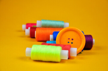 Set of buttons and Spools with multicolored threads on a yellow background. Blurring background.