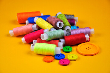 Set of buttons and Spools with multicolored threads on a yellow background. Blurring background.