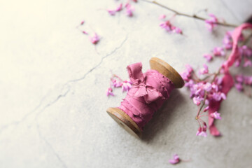 Close up of Wooden Spool Wrapped with Mauve-Pink Silk Ribbon with Red Bud Blossoms