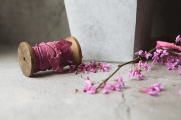Naklejka premium Close up of Wooden Spool Wrapped with Mauve-Pink Silk Ribbon with Red Bud Blossoms