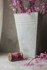 Wooden Spool of Mauve-Pink Silk Ribbon beside a Tin Vase of Red Bud Branches