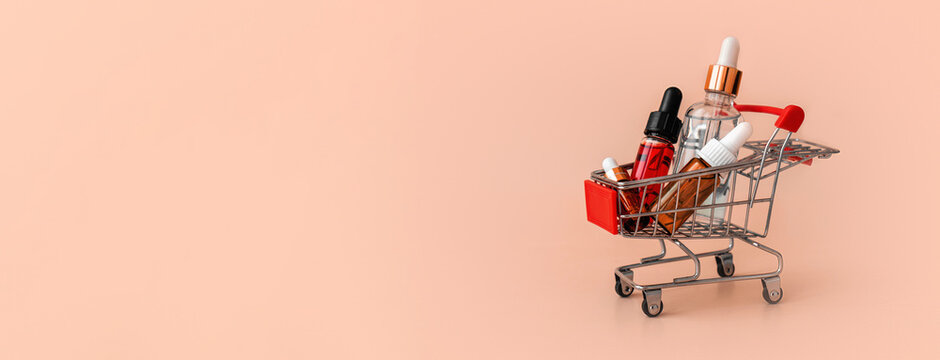 Online shopping minimalistic concept. Small cart with cosmetic bottles. Essential oil, serum and peeling gel in glass droppers. Mixture of beauty products.