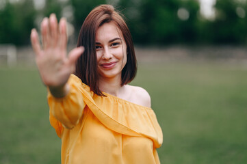 Brunette with a Smile on her Face put her palm forward, Portrait on a Natural Background