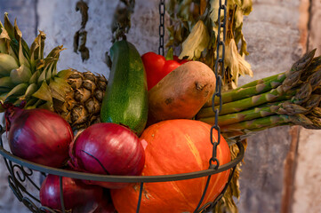 Hanging basket with various fresh ingredients for cooking such as pumpkin, zucchini, sweet potato and red onion.