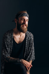 portrait of a guy with a beard and tattoos on a dark background. hipster