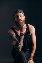 portrait of a guy with a beard and tattoos on a dark background. hipster