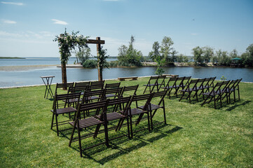 Wedding Arch and wooden chairs on the background beautiful river. Summer day