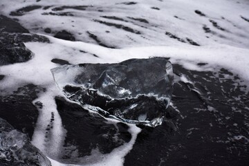 Detail of a piece of iceberg from the glacier drift ashore on the black volcanic sand of the...