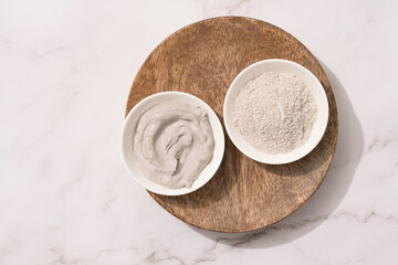 Bowl with gray cosmetic clay cream and clay powder on wooden tray - mineral bentonite facial mask. Skincare beauty concept. Selective focus. Top view