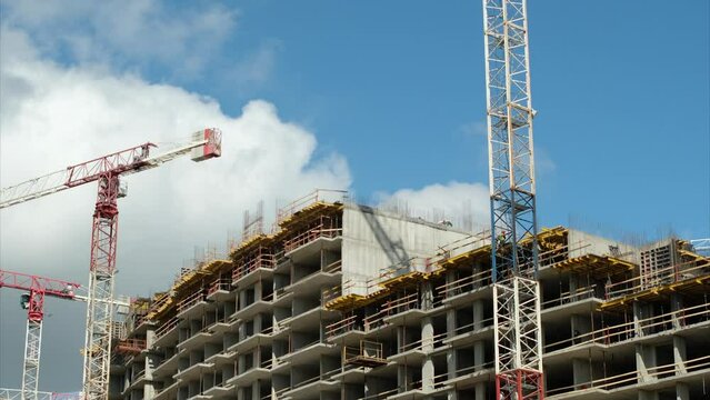 Tower cranes operate at construction site during day against cloudy sky. Process of upper floors building in new residential district in city time lapse