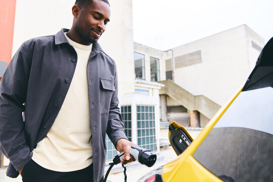 Man Plugging In Electric Car Outside Office In Car Park Charging