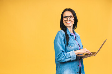 Portrait of happy young beautiful surprised woman with glasses standing with laptop isolated on yellow background. Space for text. - 511121221