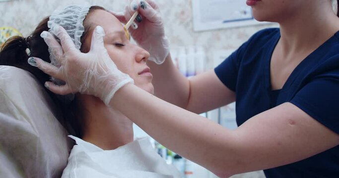 Eyebrow correction master removes excess hairs with wax and tweezers, close up