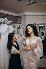 Naklejka premium Bride at the clothes shop for wedding dresses. she is choosing a dress and the designer are assisting her