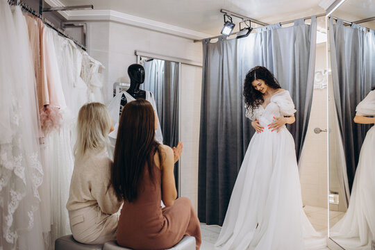 Woman trying on wedding dress with female friends having fun and taking photographs.
