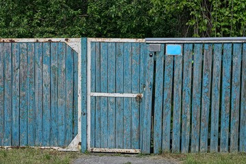 Blue old wooden fence and closed doors on the rural street near the road