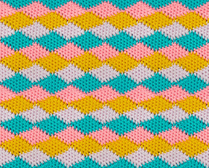 Geometric seamless knitted pattern. The texture is crocheted from multi-colored yarn. Repeating rhombuses.