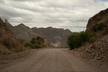 Travel. View of the dirt road across the desert and mountains under a cloudy sky.