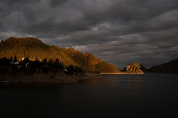 View of the rocky mountains and lake under a dramatic sky, at sunset in Los Reyunos, Mendoza, Argentina.	