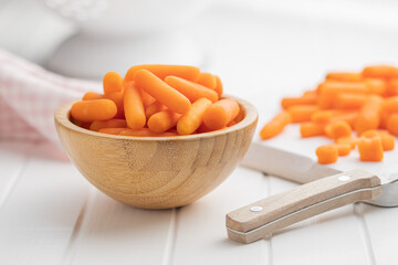Baby carrot vegetable in bowl. Mini orange carrots on white table.