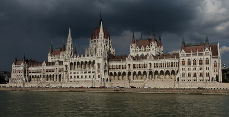 Obraz premium Parliament in Budapest viewed across the river Danube. Dark sky, heavy clouds.