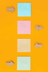 Colorful sticky notes and different wooden arrows on yellow background.