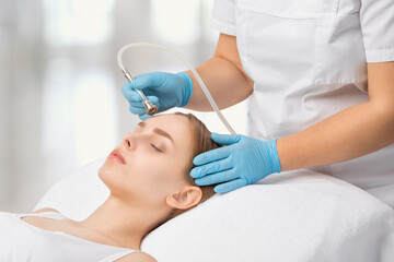 Fototapeta premium Cosmetologist makes procedure microdermabrasion on the face against acne and blackheads near the eyes. Women's cosmetology in the beauty salon.