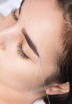 The make-up artist plucks eyebrows with a thread close-up. Women's cosmetology in the beauty salon.