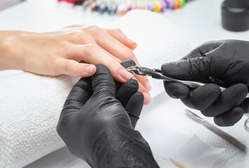 A manicurist removes cuticles during a nail extension procedure in a beauty salon. Professional...