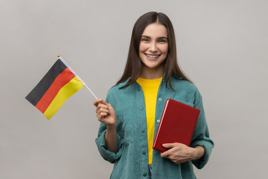 Portrait of attractive smart optimistic woman holding in hands book and german flag, education courses abroad, wearing casual style jacket. Indoor studio shot isolated on gray background.