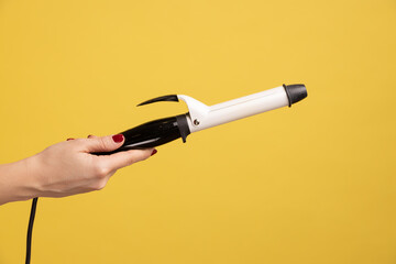 Closeup side view of woman hand holding showing iron curler, professional curling tongs, beauty...