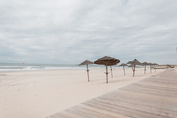 Empty sandy beach with a wooden walkway and straw umbrellas near the ocean. Vacation in Portugal. Atlantic Ocean. Vacation at sea.