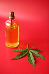 A bottle of cbd oil and marijuana leaf against red background