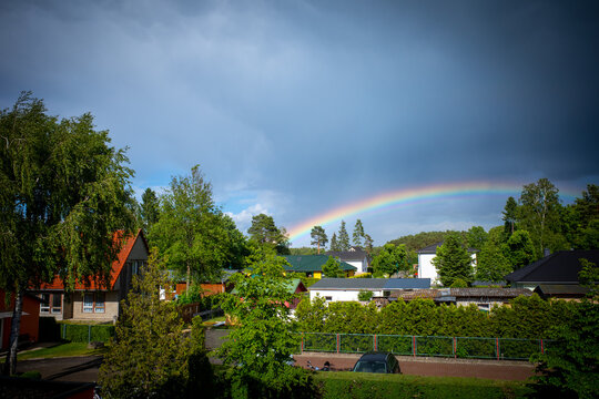 Over A Residential Area Is A Large Colorful Rainbow