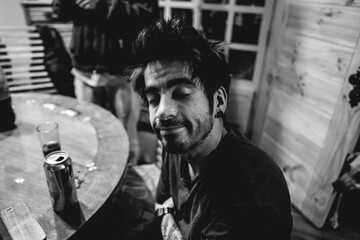 Young and handsome guy smiling in front of a wood table with a beer can and a glass in the dining room (in black and white)