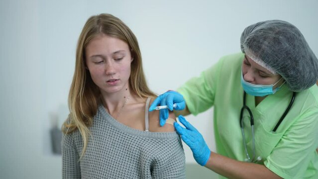 Happy teenage girl gesturing thumb up getting Covid-19 vaccine shot looking at camera smiling. Portrait of satisfied Caucasian patient posing in vaccination center advertising drug