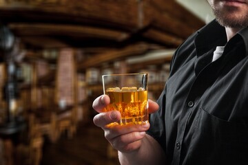 Man with elegant glass of brandy on the bar counter. Alcoholic drinks, cognac, whiskey, port, brandy, rum, scotch, bourbon. Vintage wooden table in a pub at night.