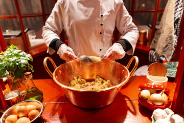 Female chef cook works in a restaurant and makes a delicious traditional dish with spoons. Girl in the robe makes a Portuguese fish cutlet, the codfish cake